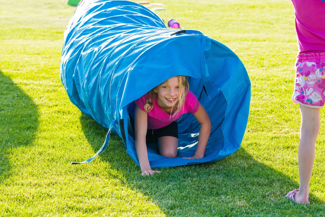 girl crawling through a blue fabric play tunnel in a park